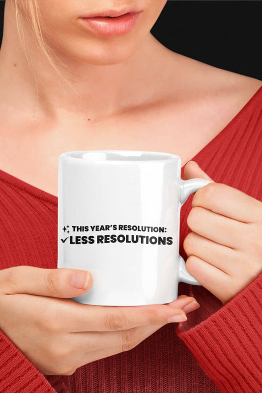 Funny new year coffee mug with a person holding a white mug with humorous text 'This year’s resolution: Less resolutions.' in a red sweater.