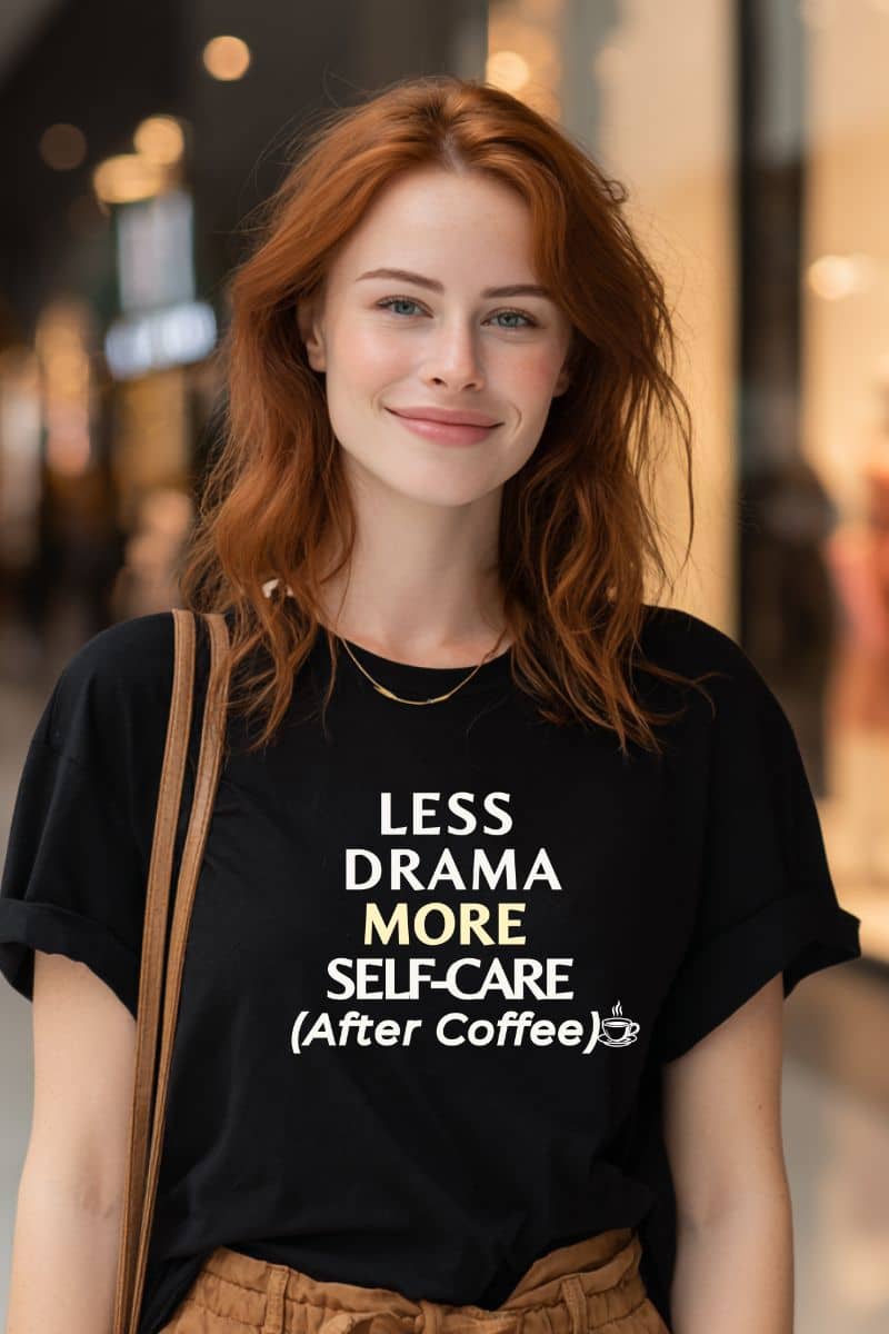 Funny office shirts with a woman wearing a black t-shirt with text 'Less Drama, More Self-Care (After Coffee)' on it, standing in an urban setting.