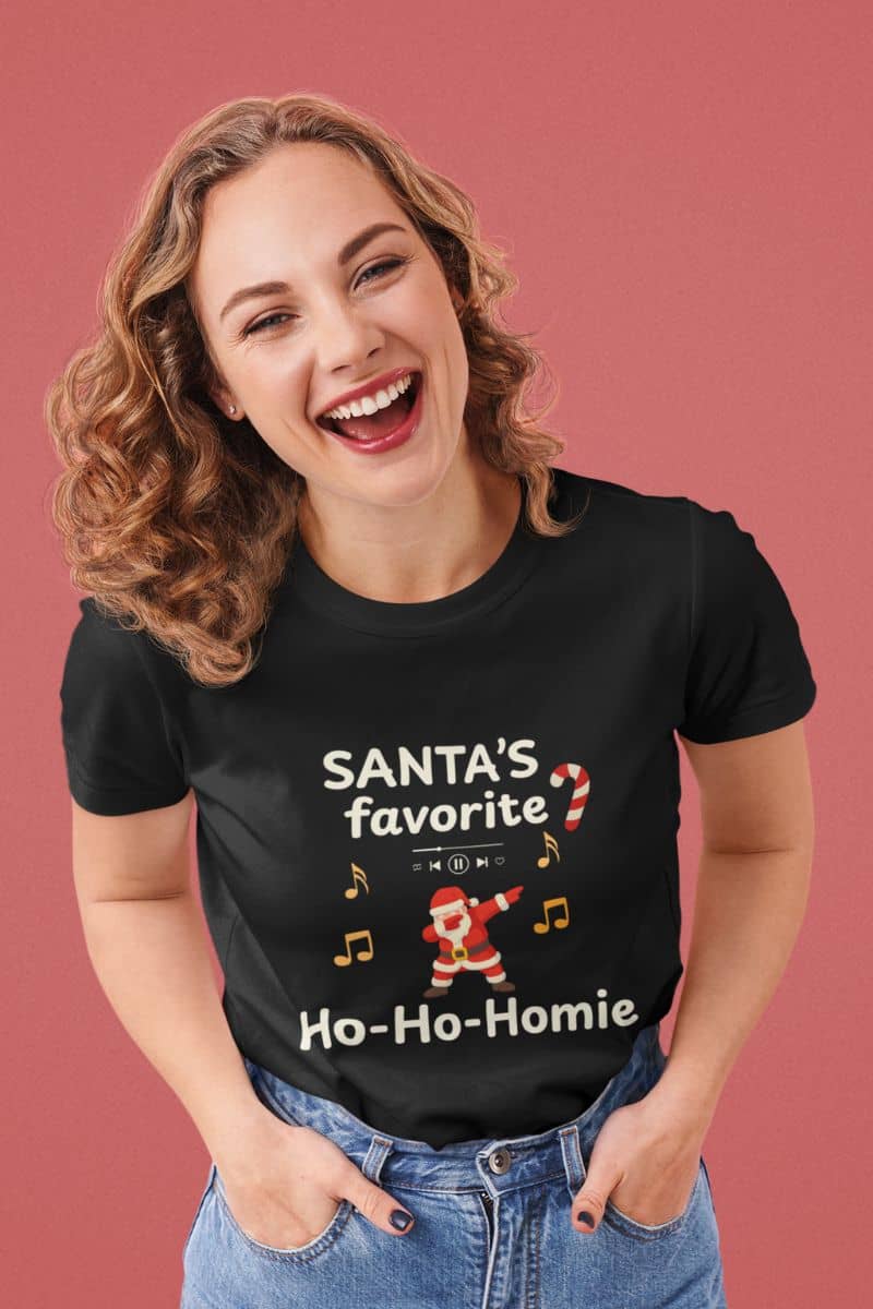 Funny santa christmas t-shirt with a woman wearing a black t-shirt text 'Santa's Favorite Ho-Ho-Homie' on a pink background