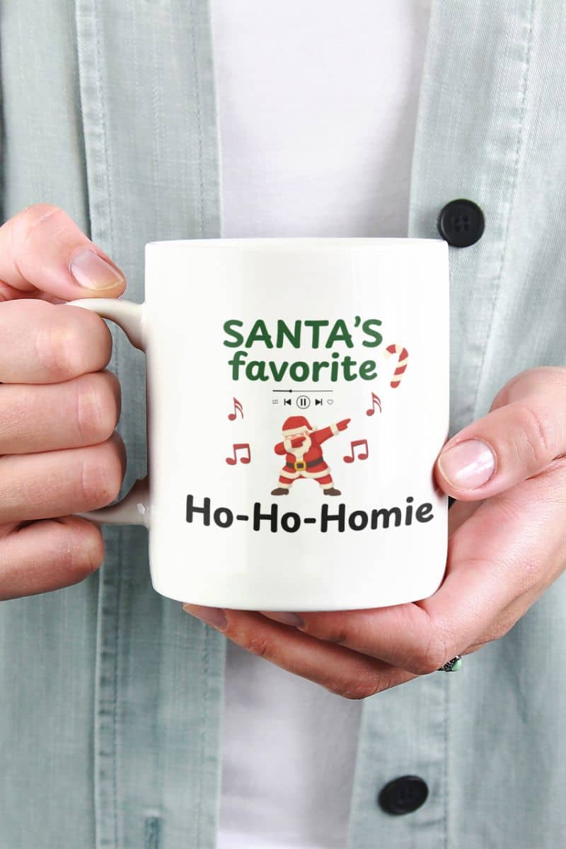 Funny santa coffee mug with a person holding a mug with 'Santa's favorite Ho-Ho-Homie' text and Santa Claus graphic.