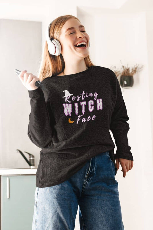 Funny witch pullover with a person wearing a black sweatshirt with 'Resting Witch Face' text, laughing in a kitchen.