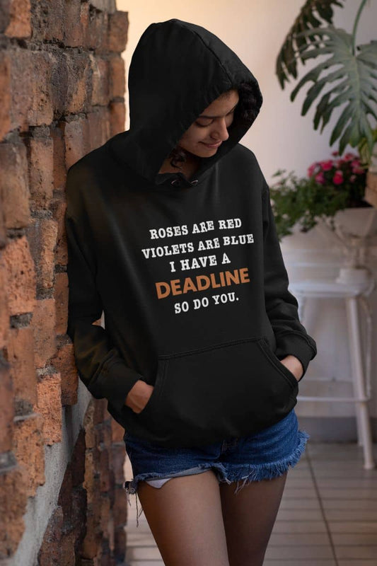 Funny work hoodie with a person wearing a black hoodie with text 'Roes are red, violets are blue. I have a deadline so you do' leaning against a brick wall.