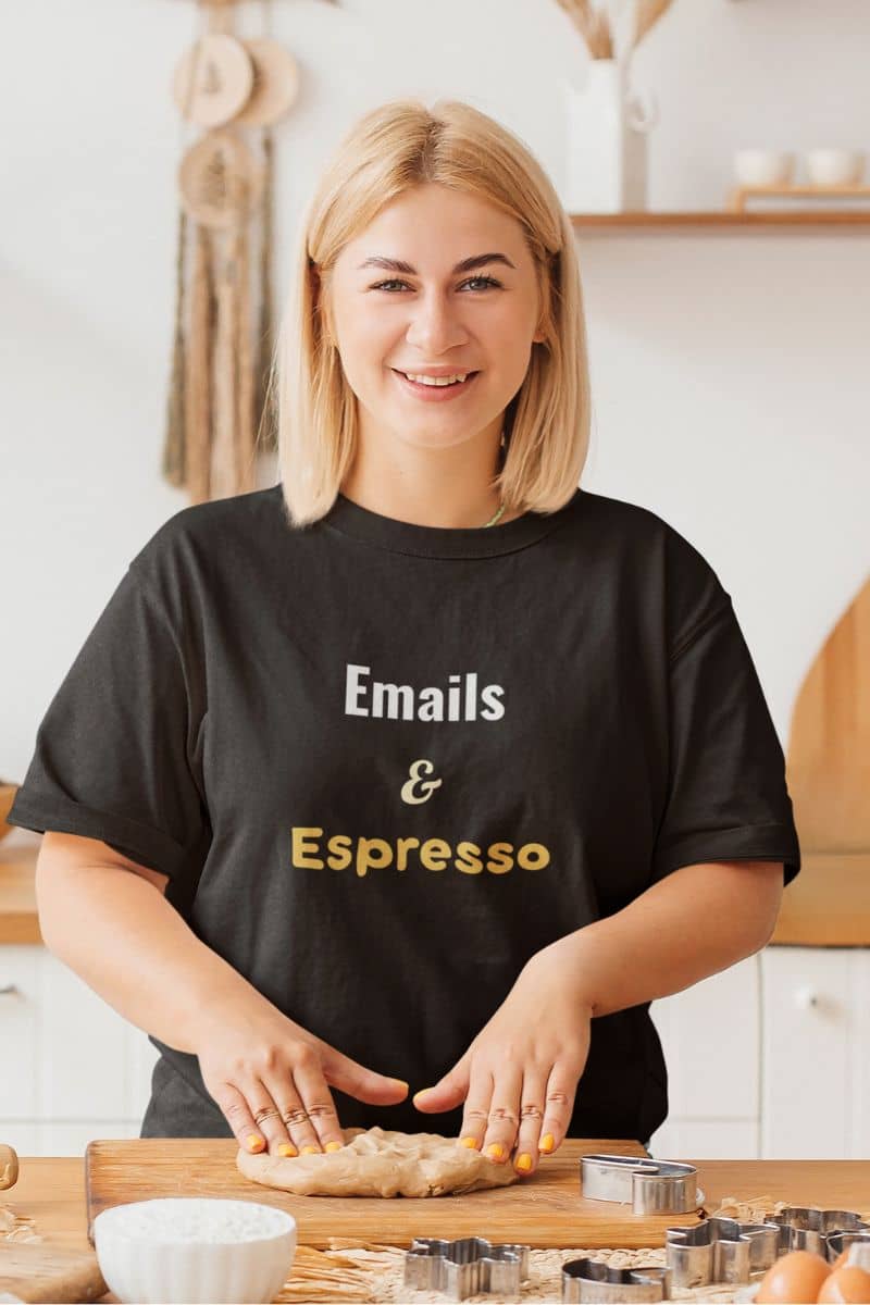 Funny workplace t-shirt with a woman in a kitchen wearing a black t-shirt with 'Emails & Espresso' text.