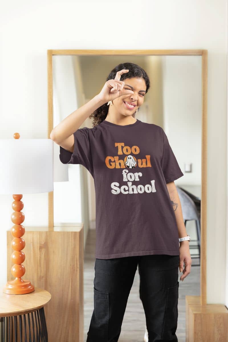 Ghost halloween t-shirt with a person wearing a 'Too Ghoul for School' t-shirt in a room with a mirror and lamp.