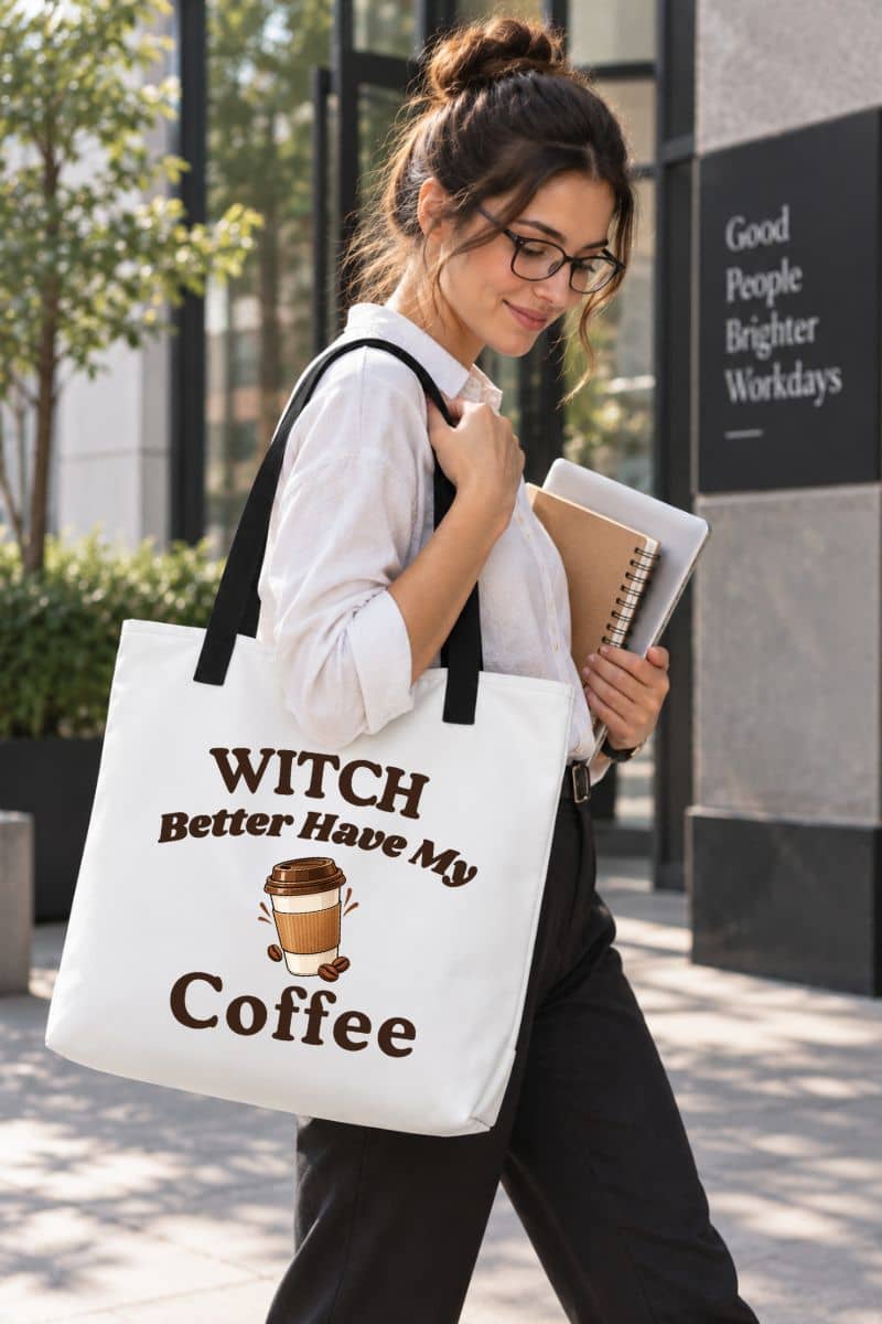 Halloween coffee tote bag with a woman walking outdoors carrying a white canvas tote bag with black handles and the printed phrase 'Witch Better Have My Coffee' along with a coffee cup graphic.
