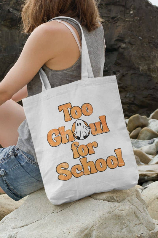 Halloween tote bag with a person holding a tote bag with 'Too Ghoul for School' text and ghost graphic on rocks.