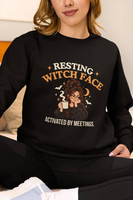 A woman wearing a Halloween witch sweatshirt featuring the text 'Resting Witch Face. Activated by Meetings.' with a woman's face