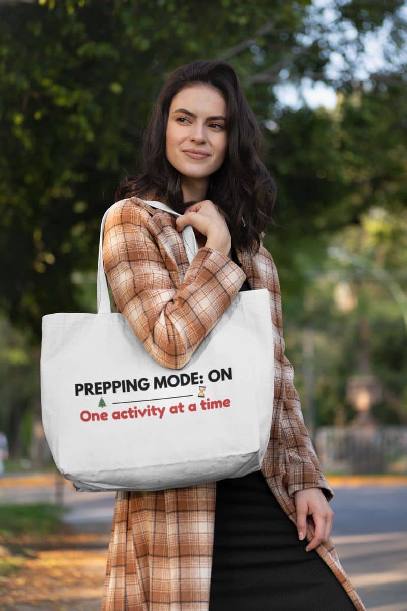 Holiday checklist tote bag with a woman holding a tote bag with text 'Prepping mode: on, One activity at a time' in an outdoor setting.