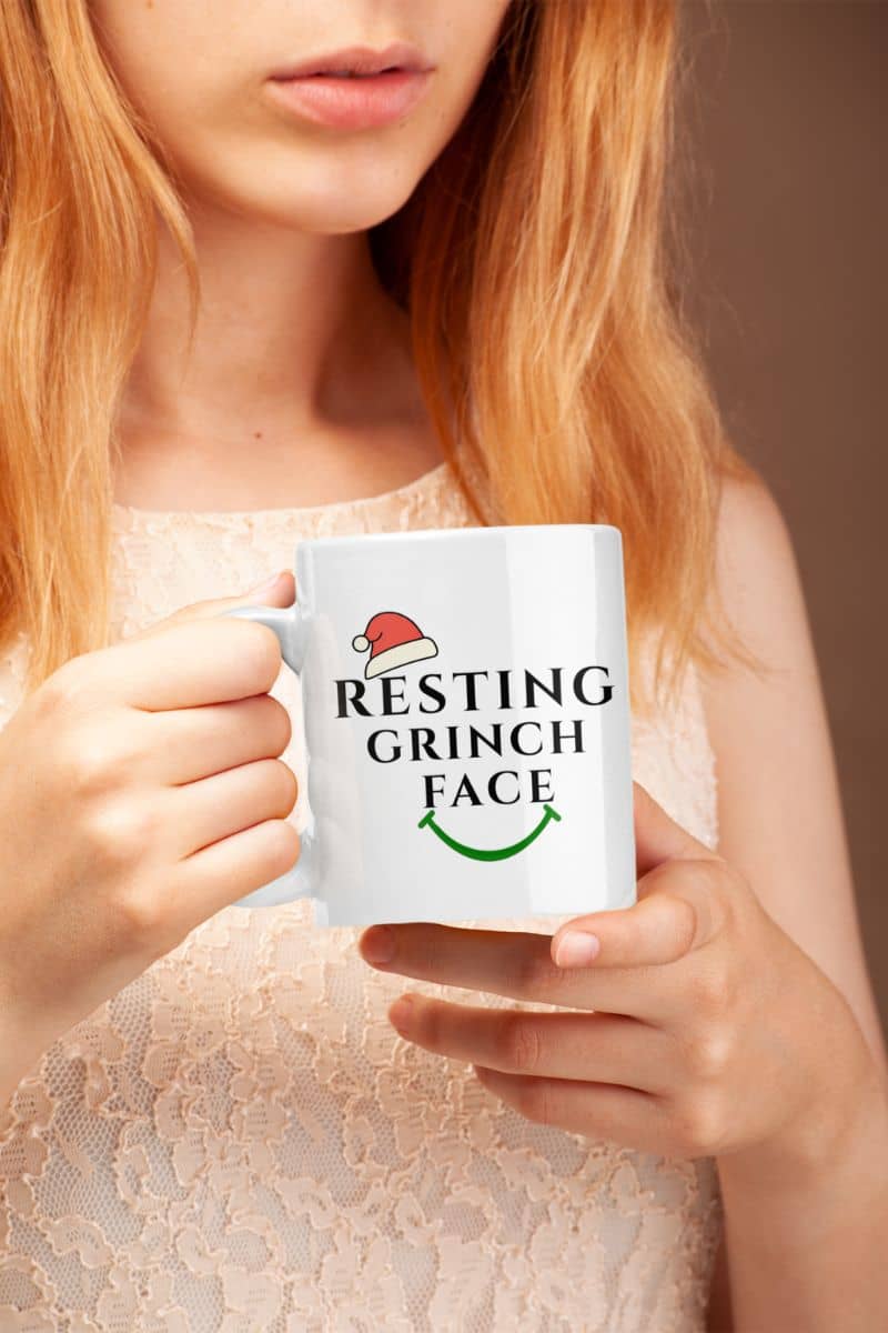 Holiday coffee cup with a person holding a mug with 'Resting Grinch Face' text and Santa hat graphic.