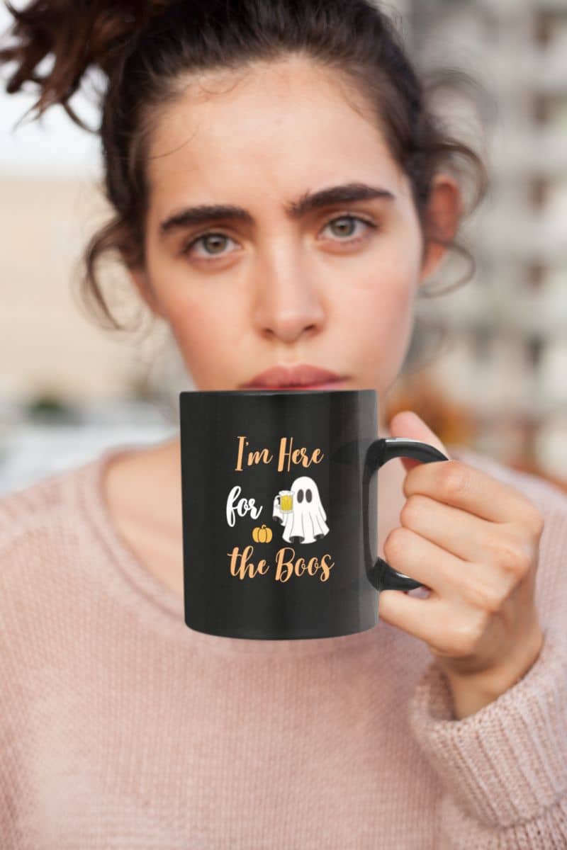 'I'm Here for the Boos' mug with a person holding a black mug with Halloween-themed text and graphics.
