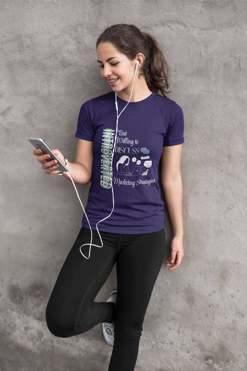 Introvert marketer tee with a girl leaning against the wall, listening to music with headphones and looking at her phone