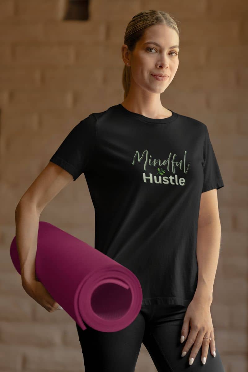 Leadership graphic tee with a woman holding a pink yoga mat wearing a black t-shirt with 'Mindful Hustle' text.