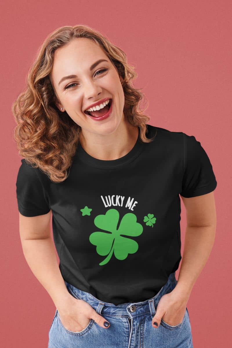 Lucky charm shirt with a woman wearing a black t-shirt with a green four-leaf clover design and 'Lucky Me' text on a pink background.
