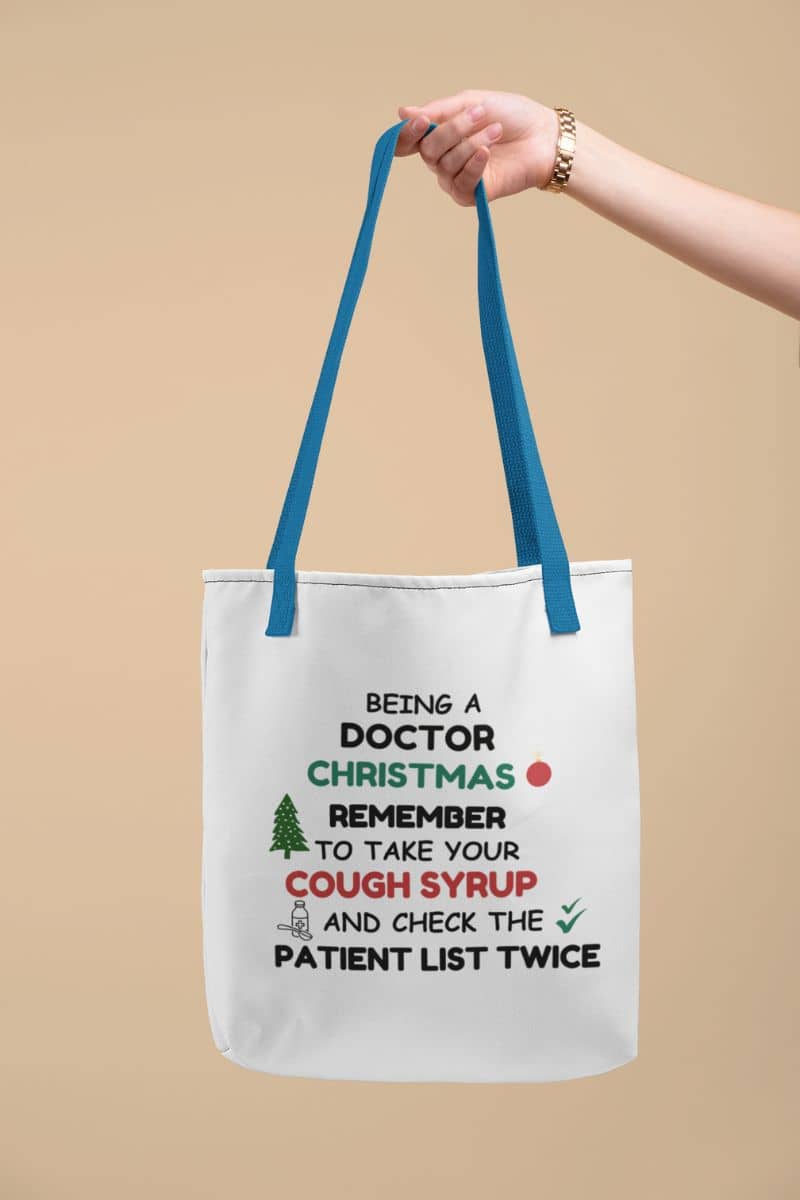 Medical Christmas tote bag with a tote bag with text 'Being a doctor during Christmas, remember to take your cough syrup and check the patient list twice' on a beige background