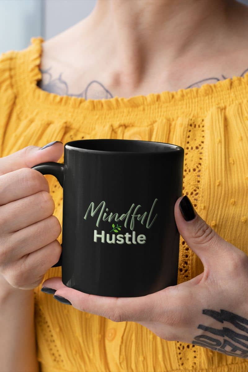 Meditation coffee mug with a person holding a black mug with 'Mindful Hustle' text, wearing a yellow top.