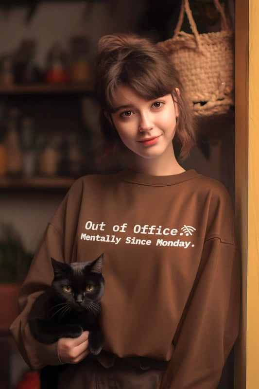 Mentally done sweatshirt with a person wearing a brown sweatshirt with text 'Out of Office. Mentally Since Monday' holding a black cat indoors.
