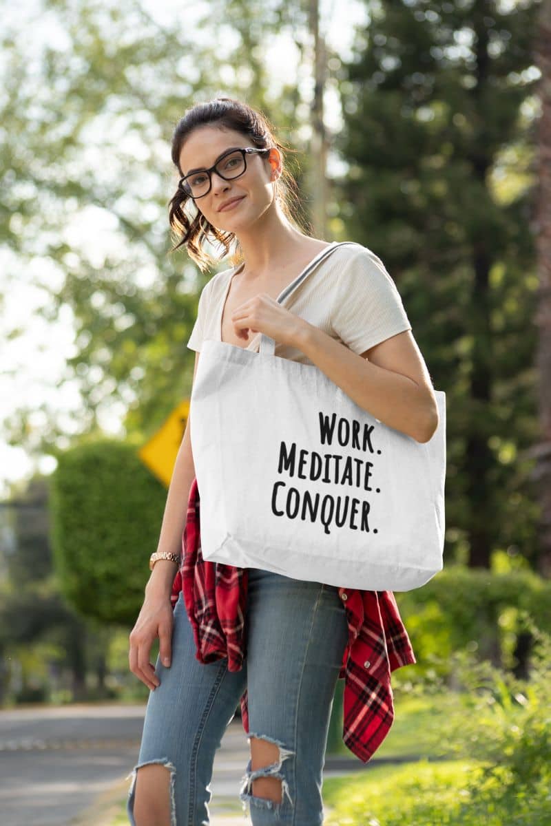 Mindful work tote bag with a woman holding a tote bag with 'Work. Meditate. Conquer.' text outdoors.