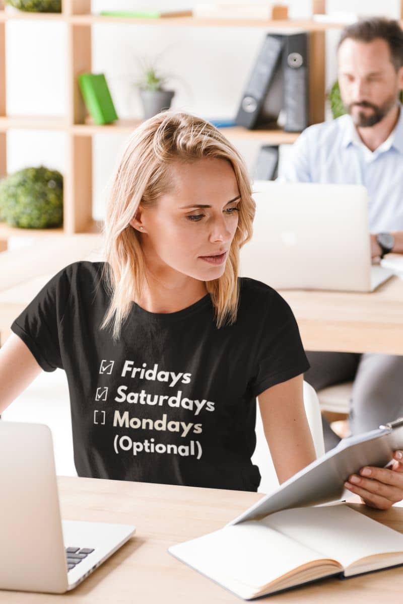 Minimalist funny shirt with a person wearing a black t-shirt with text 'Fridays and Saturdays, Mondays (Optional)' in an office setting