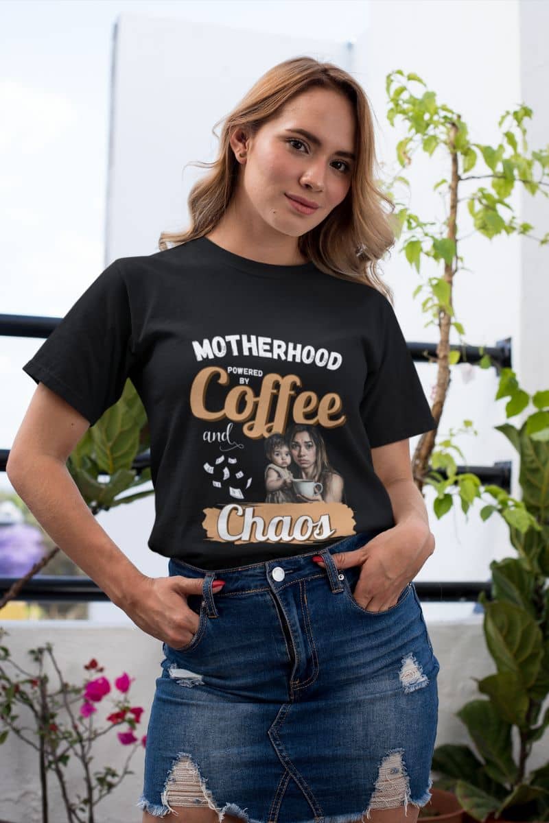 Mom humor shirt with a woman wearing a black t-shirt with 'Motherhood: Powered by Coffee and Chaos.' text and graphics.