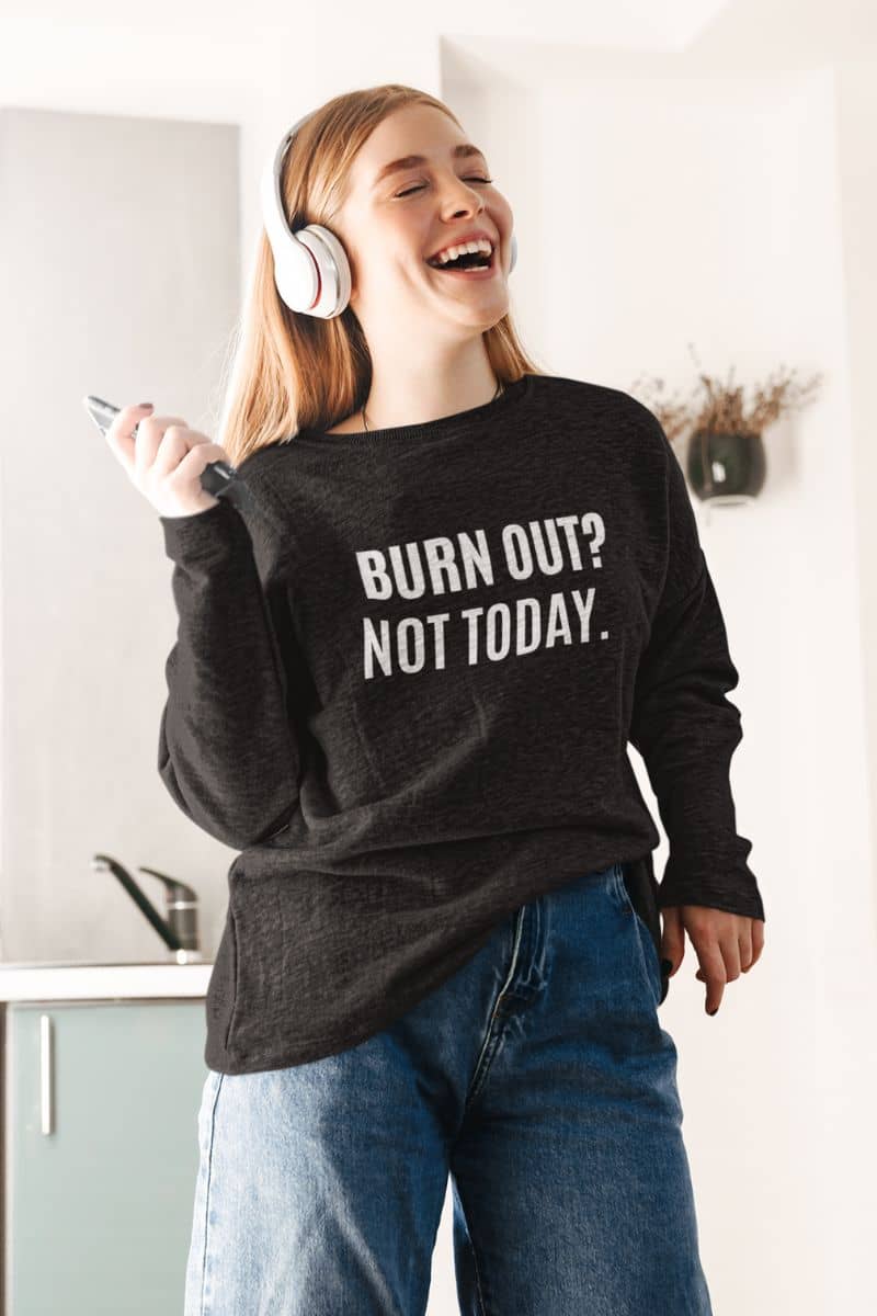 Motivational recovery sweatshirt with a person wearing a black sweatshirt with 'BURN OUT? NOT TODAY.' text, laughing in a kitchen.