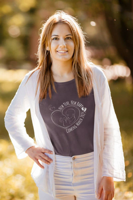 New Year, New Baby Coming March 2025 T-Shirt with a beautiful woman poses with a beautiful woman poses with a t-shirt announcing that she is expecting a baby in 2025.