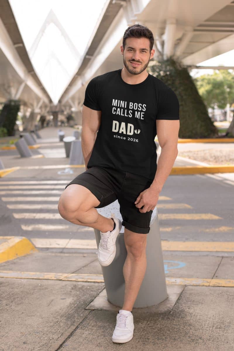 New dad shirts with a man wearing a black t-shirt with text 'Mini Boss Calls Me Dad – since 2026' standing on a street.