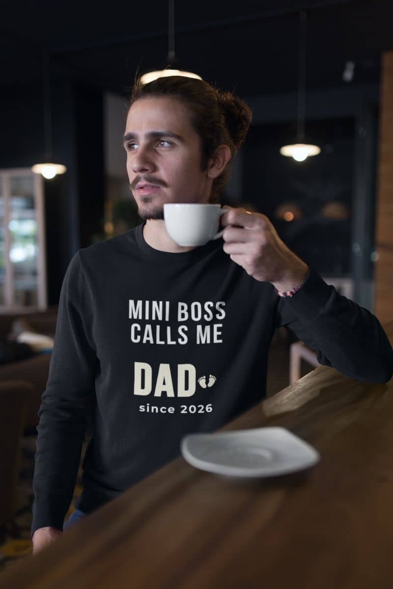 New dad sweatshirt with a man holding a cup with text 'Mini Boss Calls Me Dad since 2026' in a dark setting.