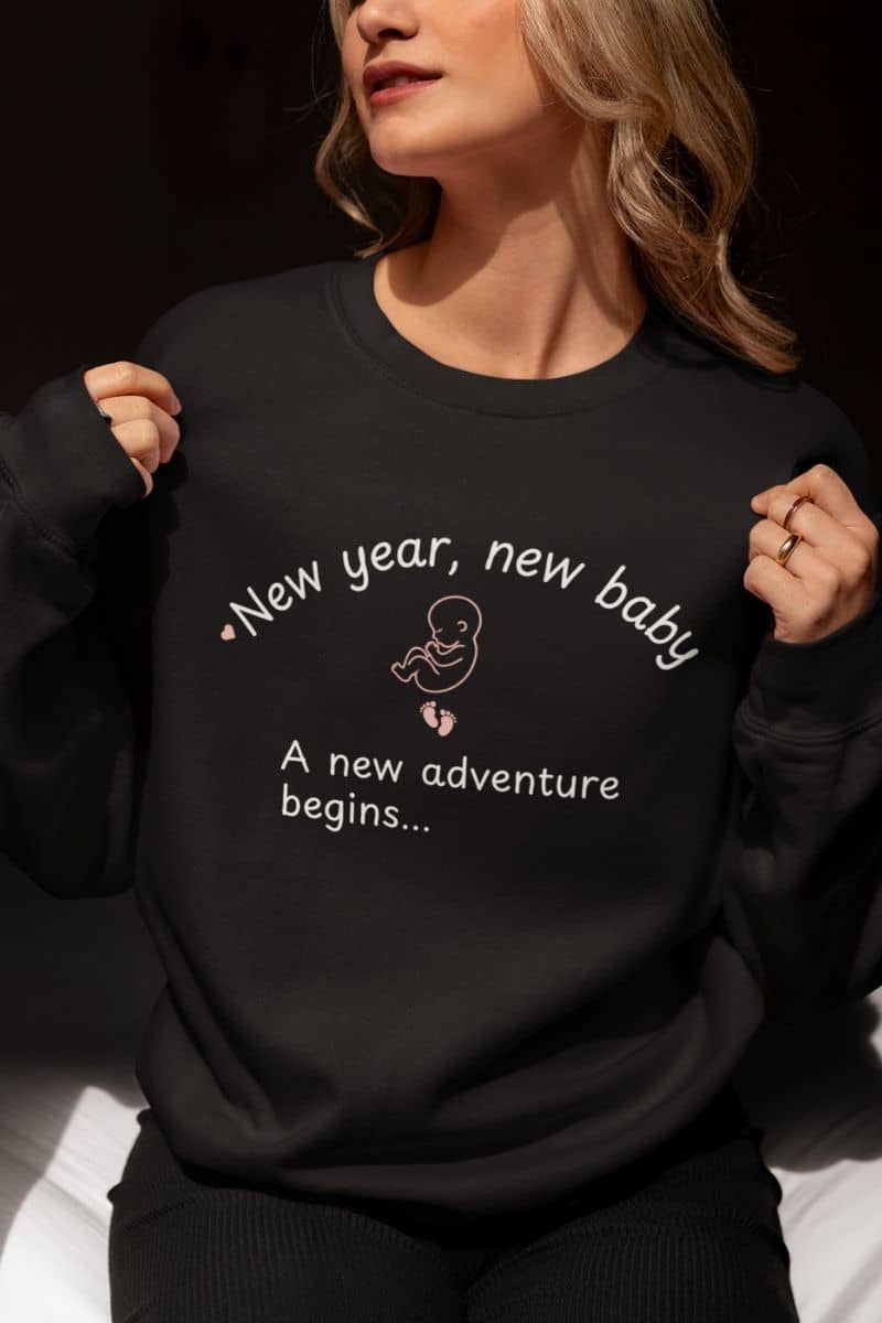 New parent sweatshirt with a woman wearing a black sweatshirt with text 'New year, new baby. A new adventure begins...'
