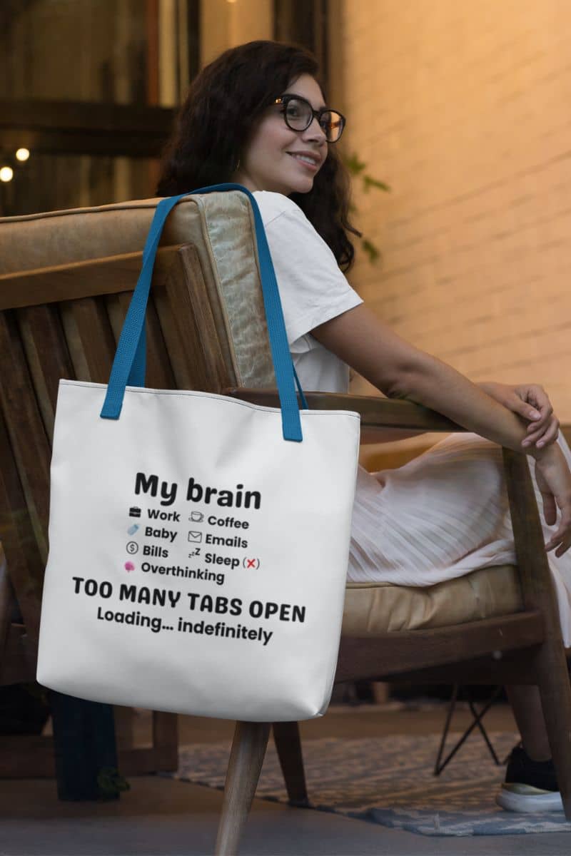 Overthinking tote bag with a white tote bag featuring the text 'My brain has too many tabs open. Loading… indefinitely.', hanging on a chair