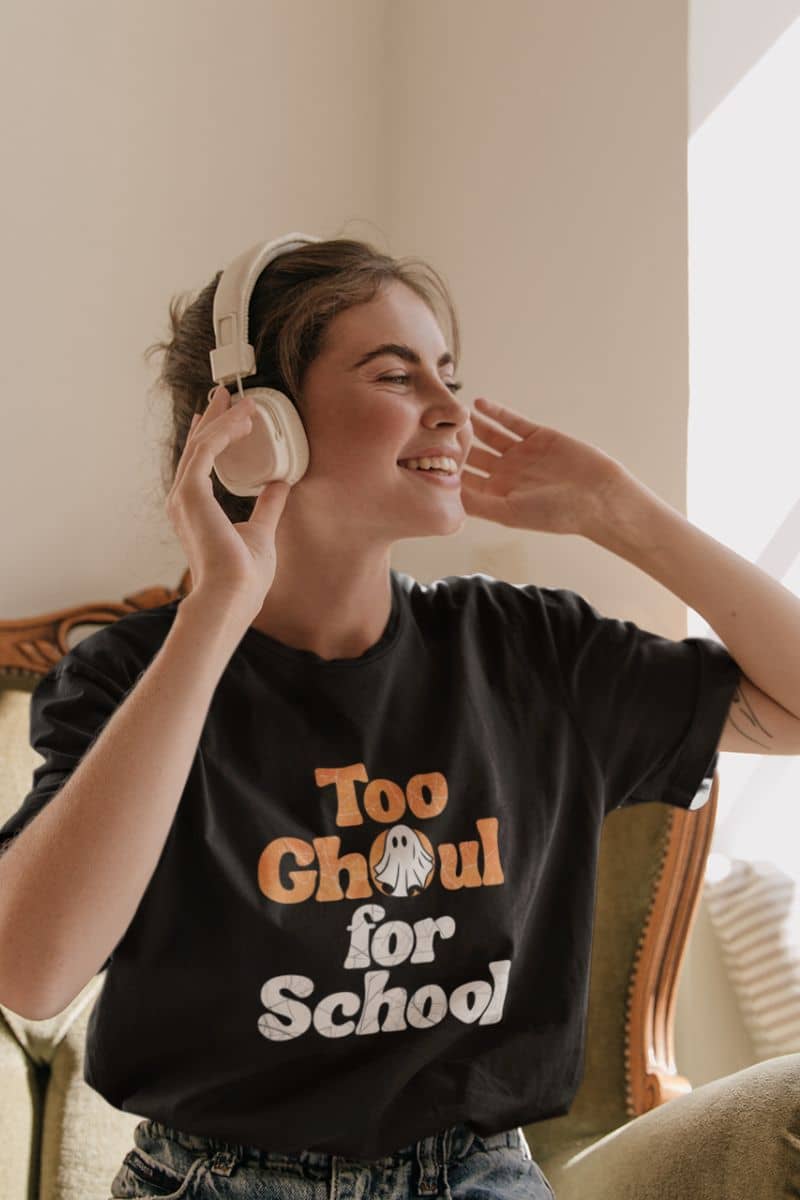 Pumpkin graphic tee with a person wearing headphones and a black t-shirt with 'Too Ghoul for School' text, sitting indoors.