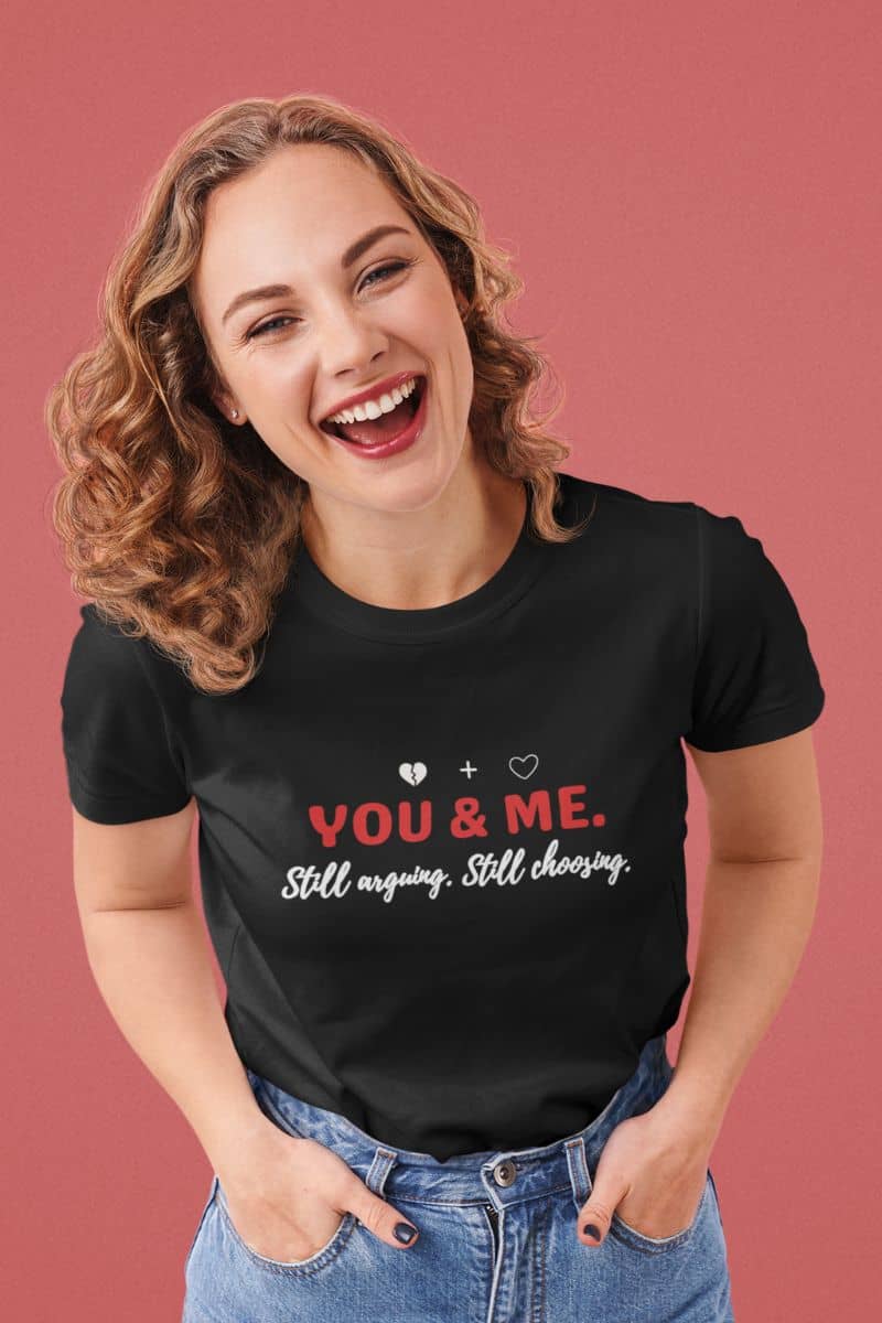 Relationship reality t shirt with a woman wearing a black t-shirt with 'YOU & ME. Still arguing, Still choosing.' text on a pink background