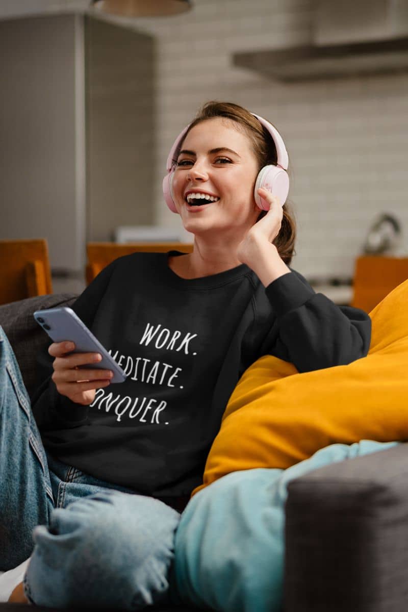 Relaxed fit meditation sweatshirt with a girl wearing headphones listening to music on the sofa with a bright smile