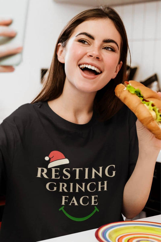 Resting Grinch Face t-shirt with a woman wearing a black t-shirt with 'Resting Grinch Face' text, holding a hot dog.