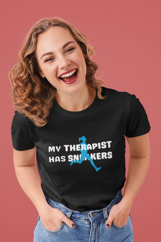 Running humor t-shirt with a woman wearing a black t-shirt with 'My Therapist Has Sneakers' text and graphic on a pink background