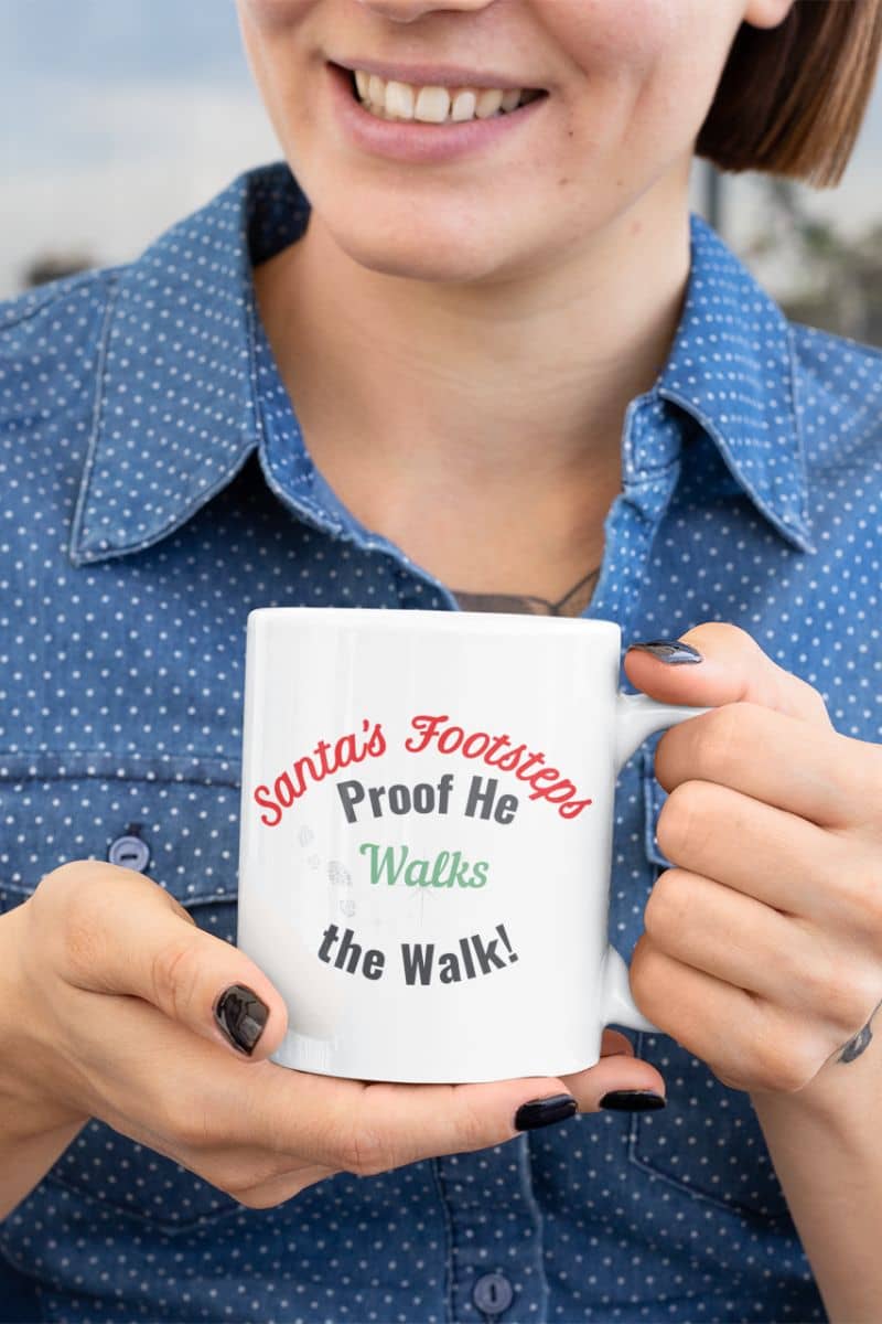 Santa footprint mug with a person holding a mug with text 'Santa's Footsteps Proof He Walks the Walk' against a blurred background
