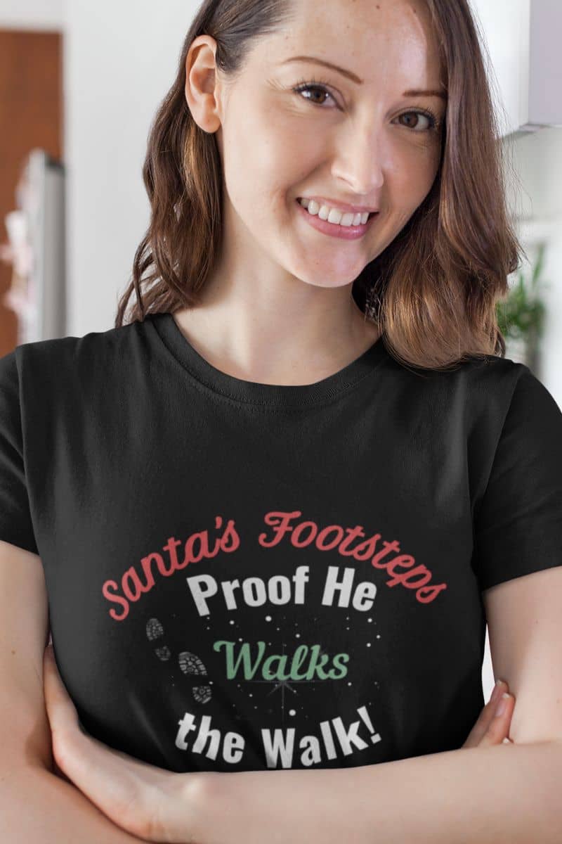 Santa footprint t-shirt with a woman wearing a black t-shirt with humorous text 'Santa's Footsteps - Proof He Walks The Walk!'