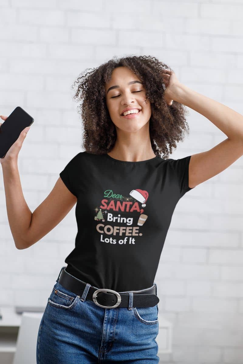 Santa graphic tee with a woman wearing a black t-shirt with a Christmas-themed design, standing against a white brick wall.