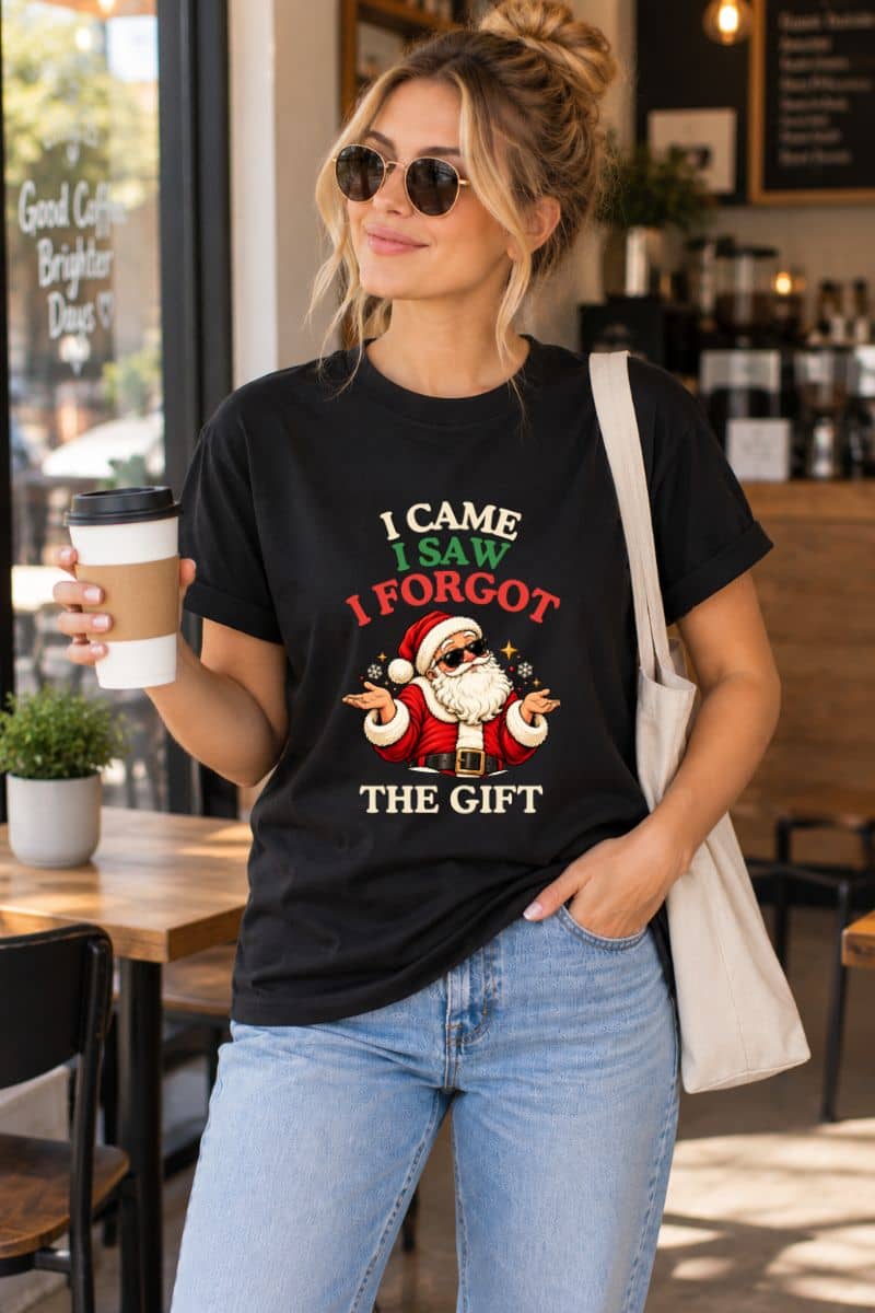 Woman wearing a black Santa Shirt with the funny “I Came. I Saw. I Forgot the Gift” design, holding takeaway coffee outside a café.