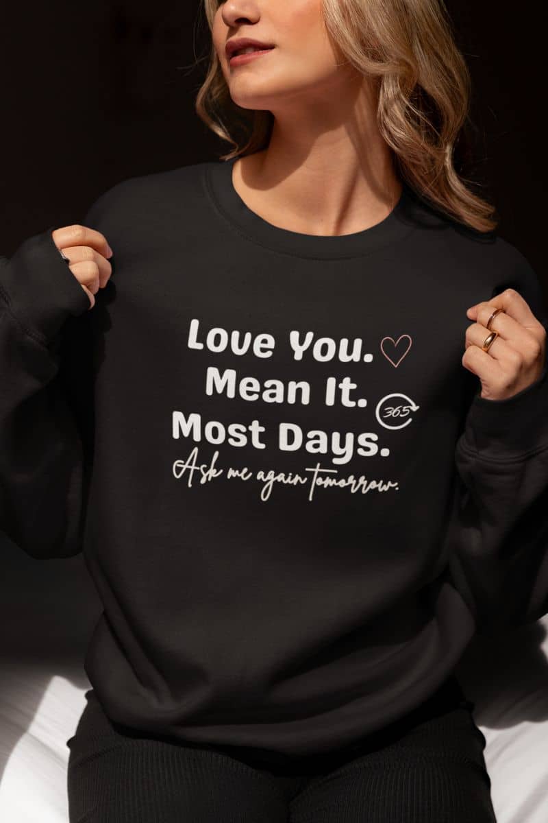 Sarcastic couples sweatshirt with a person wearing a black sweatshirt with  text 'Love You. Mean It. Most Days. Ask me again tomorrow.'