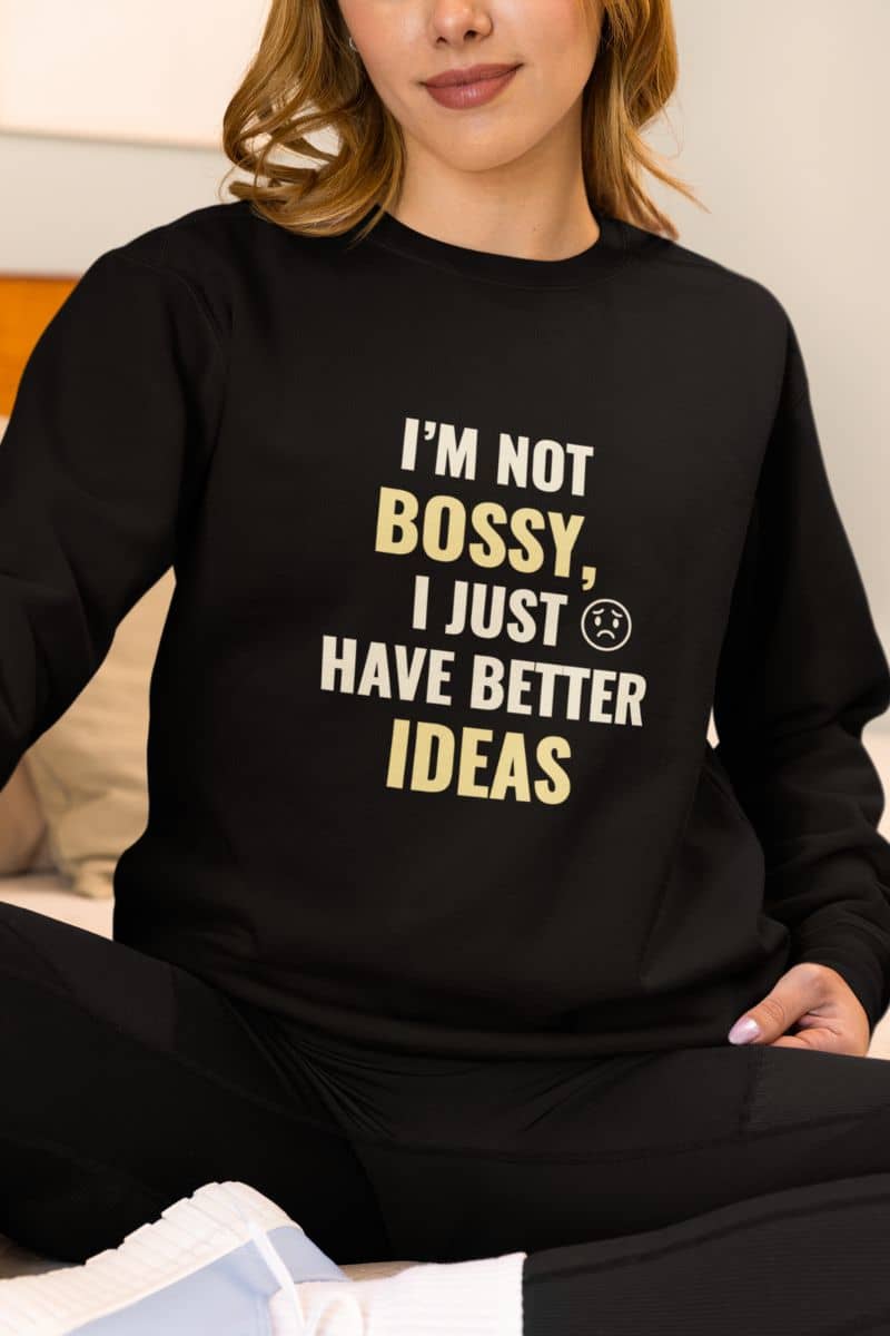 Sarcastic pullover with a person wearing a black sweatshirt with text 'I’m Not Bossy, I Just Have Better Ideas' sitting on a couch.
