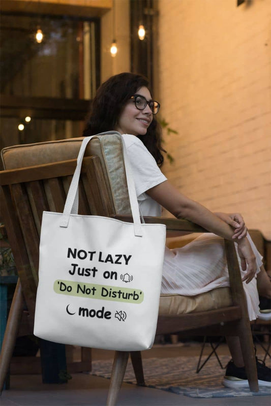 Sarcastic quiet mode tote with a woman sitting on a chair with a tote bag featuring humorous text 'NOT LAZY, Just on 'Do Not Disturb' mode'.