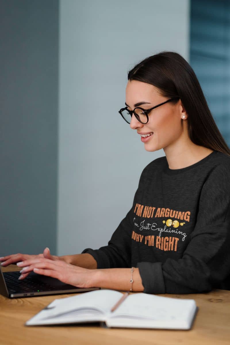 Sarcastic sweatshirt for work with girl typing on laptop next to notebook on table