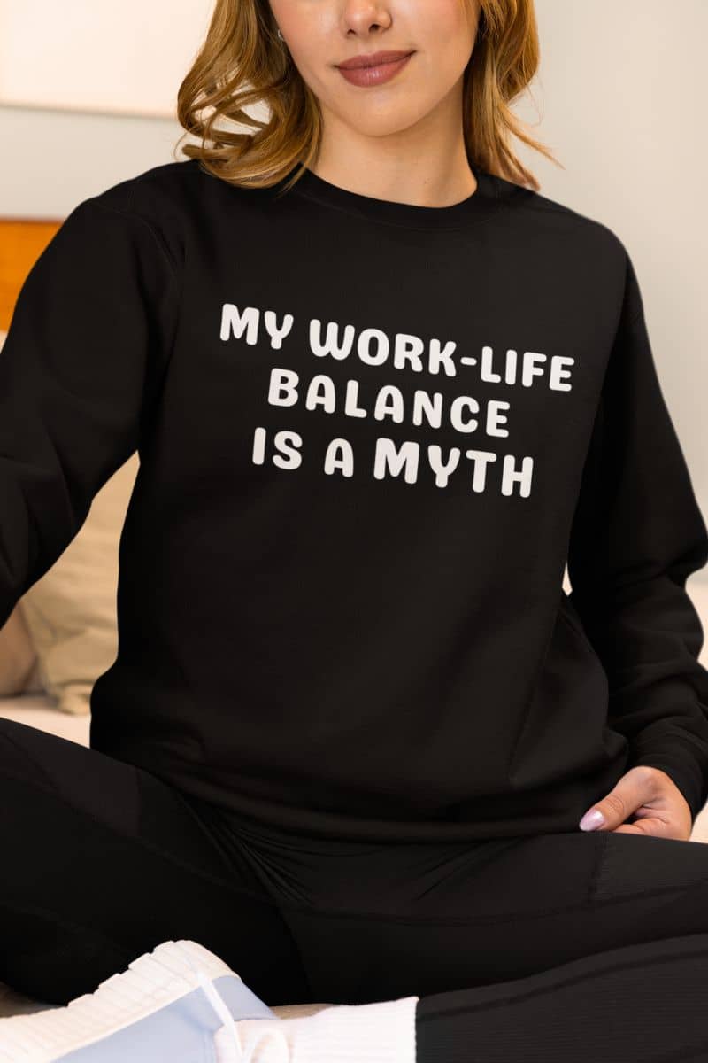 Sarcastic work quote sweatshirt with a person wearing a black sweatshirt with text 'My work-life balance is a myth'.