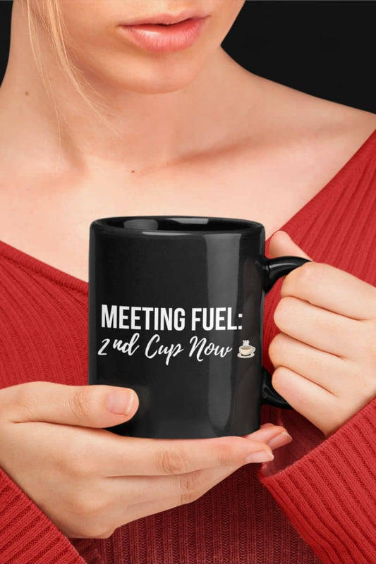 Sassy coffee mug with a person holding a black mug with text 'MEETING FUEL: 2nd Cup Now' against a black background