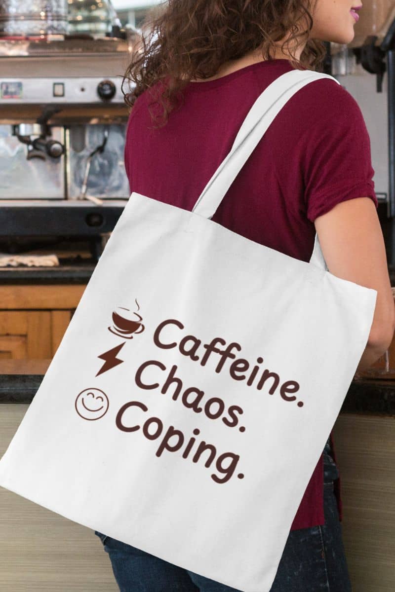 Self-care canvas bag with a person holding a tote bag with 'Caffeine. Chaos. Coping.' text in a coffee shop setting