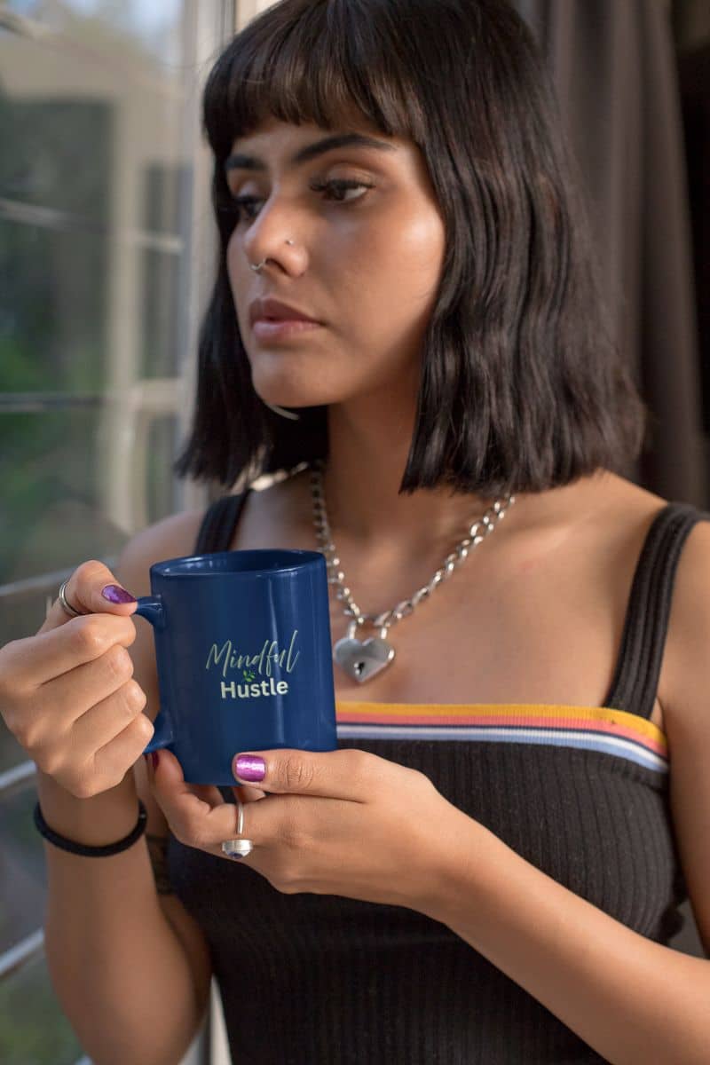 Self-care tea mug with a woman holding a blue mug with 'Mindful Hustle' text, wearing a black top and necklace.