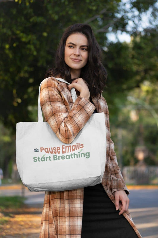 Self-care tote bag for women with a woman holding a tote bag with text "Pause Emails, Start Breathing" outdoors
