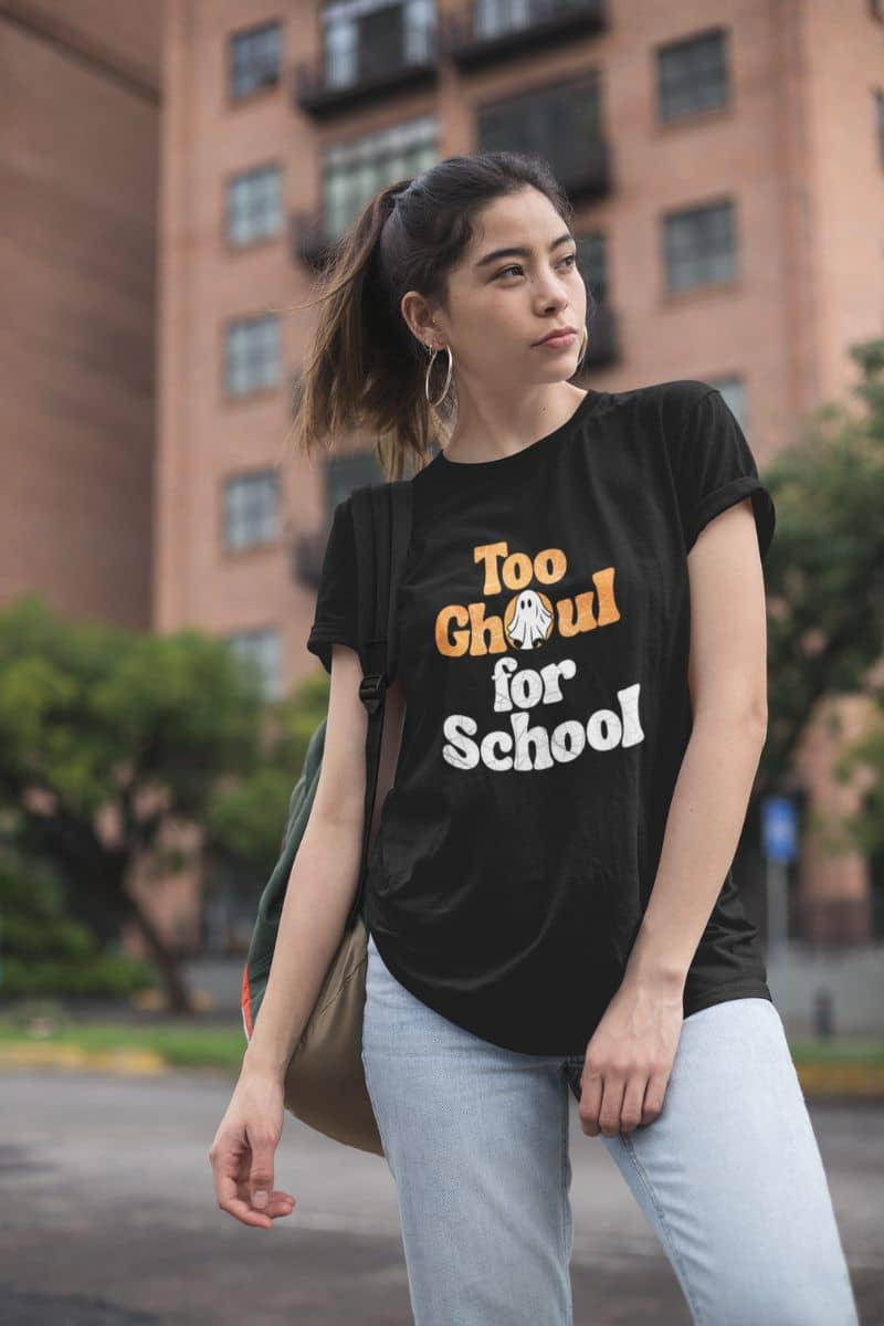 Skeleton graphic shirt with a woman wearing a black t-shirt with 'Too Ghoul for School' text, standing outdoors.