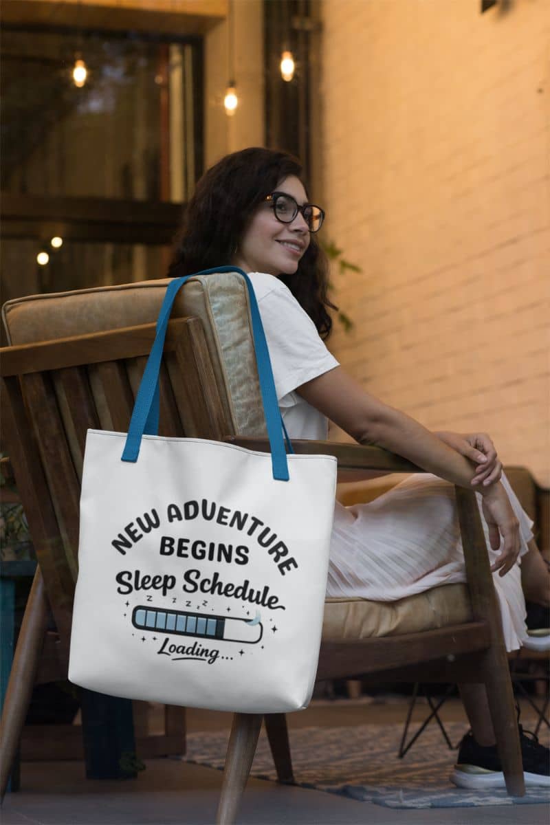 Sleep deprived tote bag with a woman sitting on a chair with a tote bag featuring text 'New Adventure Begins, Sleep Schedule Loading…'.