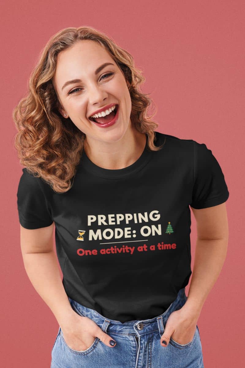 Slow holiday mode shirt with a woman wearing a black t-shirt with humorous text 'Prepping Mode: ON – One activity at a time' on a pink background